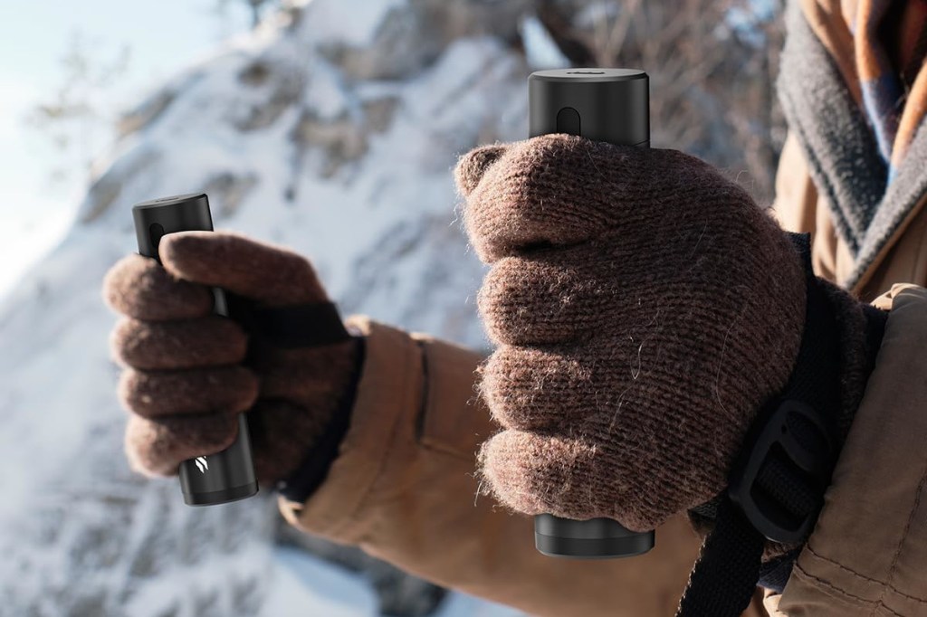 Zwei braun behandschuhte Hände halten längliche graue zylinder vor Schneekulisse