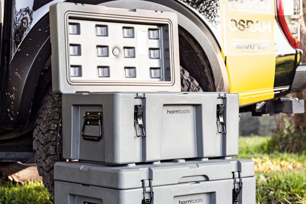 Zwei Transportboxen von Horntoools stehen übereinander vor einem Geländewagen, bei der oberrsten ist der Deckel geöffnet.