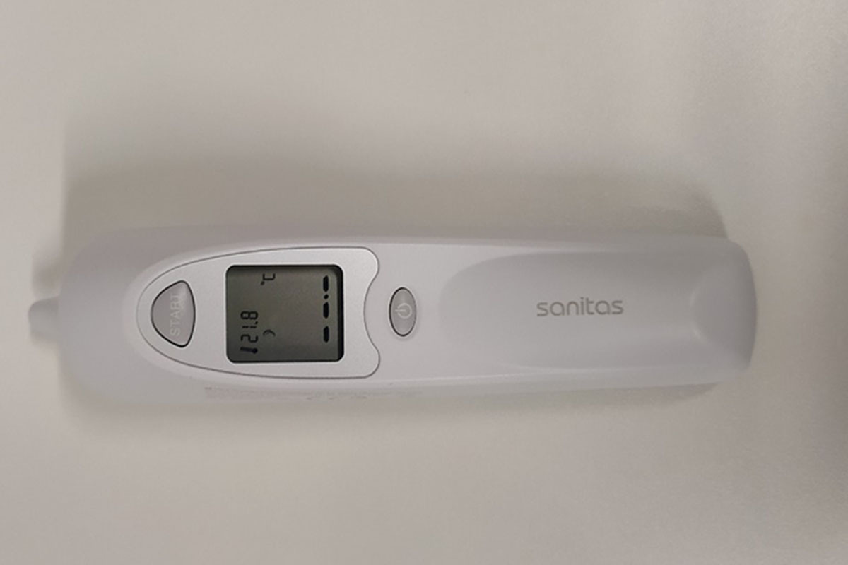 Ohrthermometer von Sanitas liegend in frontaler Ansicht mit eingeschalteten Display vor weißem Hintergrund.