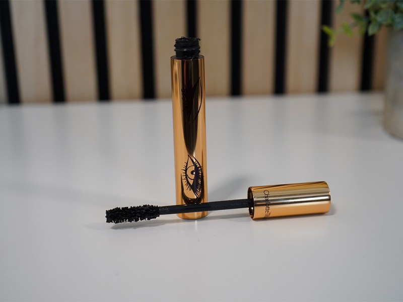 Der Mascara von Charlotte Tilbury auf einer weißer Tischplatte. Der Applikator liegt quer vor dem Wimperntusche-Behälter.