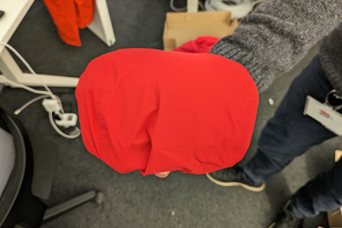 Rote Regenjacke zu kleinem Paket zusammen gefaltet in Hand eines Mannes.