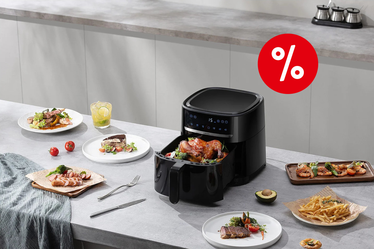 Schwarzer geöffneter Xiaomi Air Fryer mit Hähnchen im Garkorb schräg von oben auf grauer Arbeitsfläche zwischen Tellern mit gegarten Lebensmitteln mit rotem Prozentbutton rechts oben