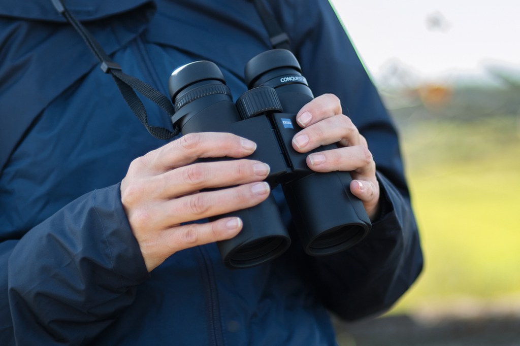 Ein Zeiss-Fernglas in Händen gehalt, von einem einem Menschen in blauer Outdoor-Jacke.