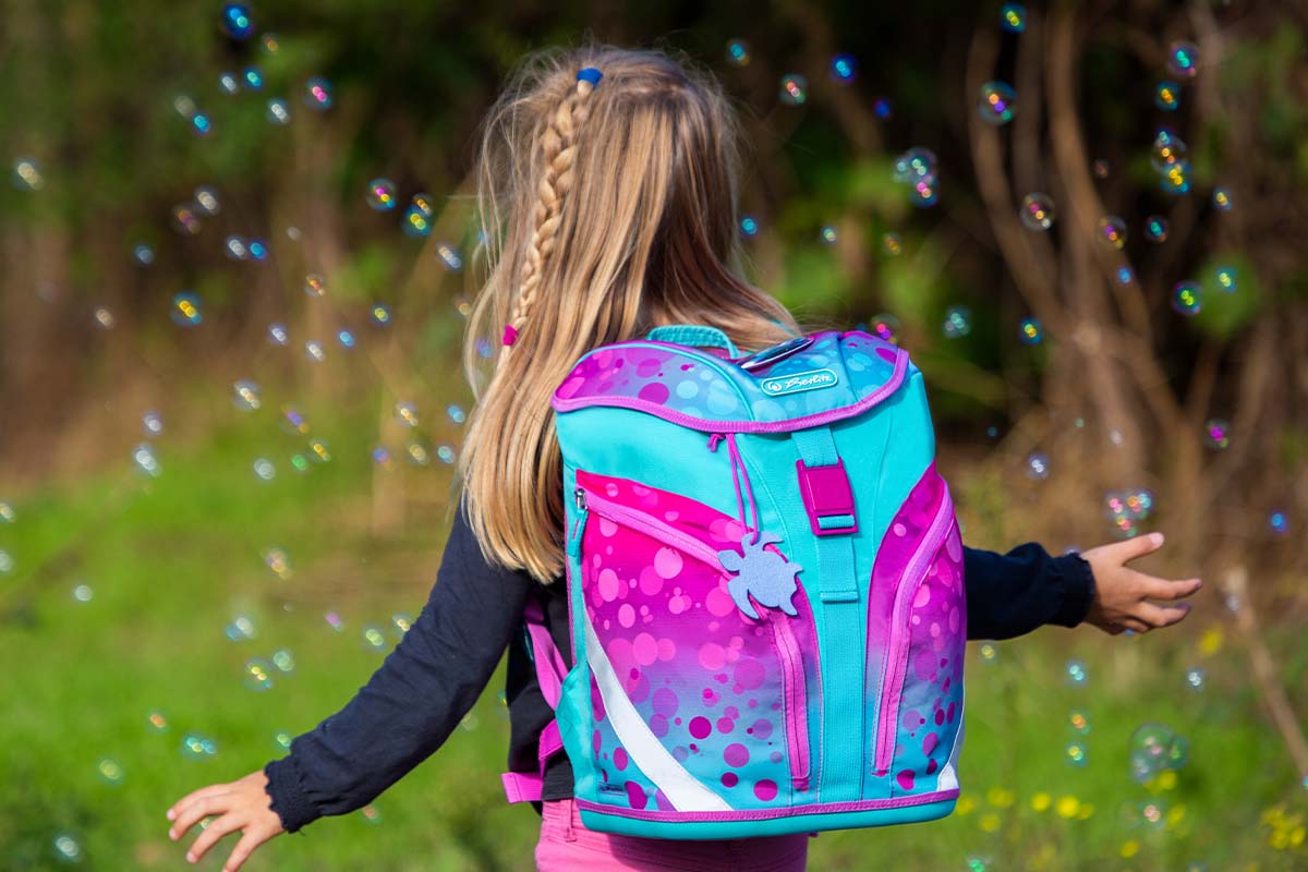 Mädchen von hinten, sie trägt einen pink-blauen Schulranzen