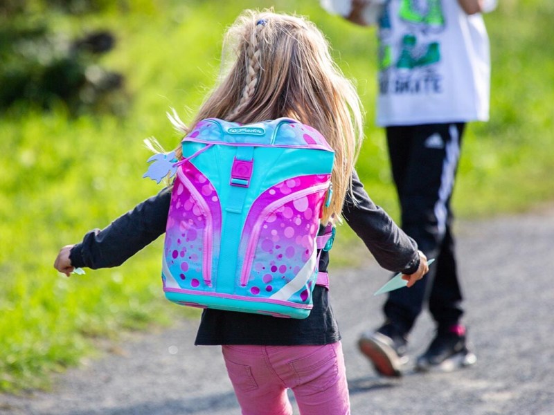 Mädchen von hinten, es trägt einen pink-türkisen Schulranzen