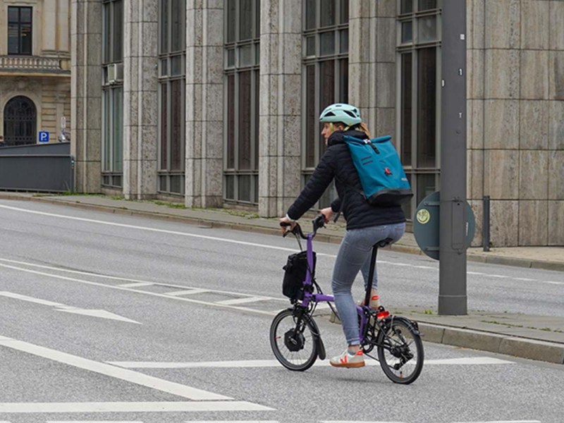 Frau von hinten, sie fährt auf einem kleinen klappfahrrad eine straße entlang