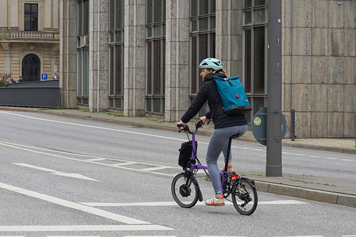 Frau von hinten, sie fährt auf einem kleinen klappfahrrad eine straße entlang