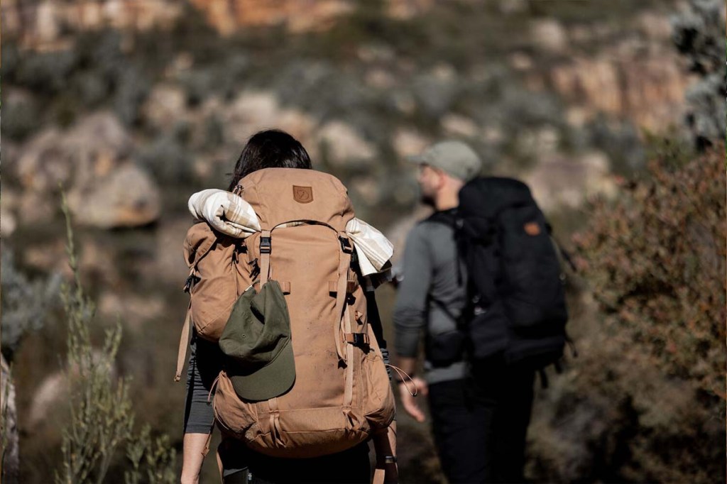 Zwei Peronen von hinten, beide mit dicken Rucksäcken, wandern durch die Natur