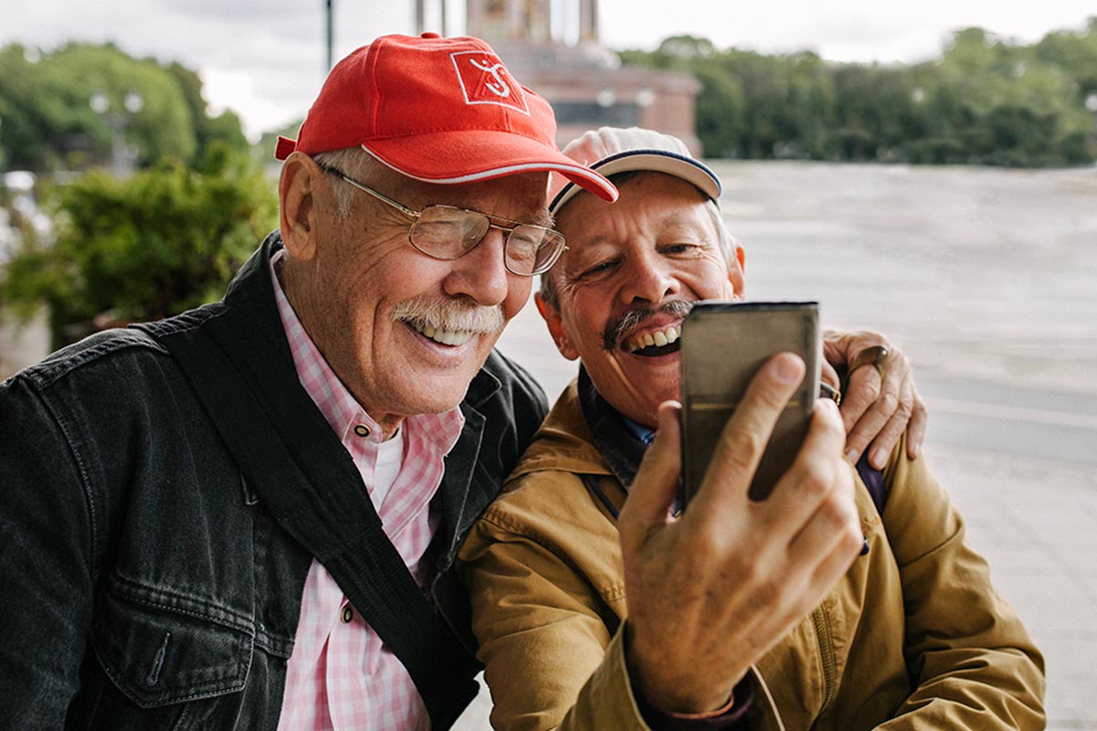 Zwei ältere Männer mit einem Smartphone in der Hand unter freiem Himmel.