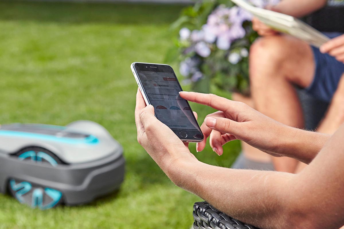 Person mit Smartphone in der Hand in einem Garten.