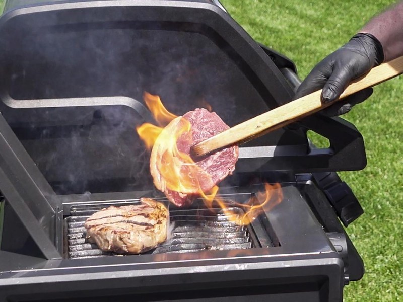 Person wendet ein Stück Fleisch auf einem Grill.