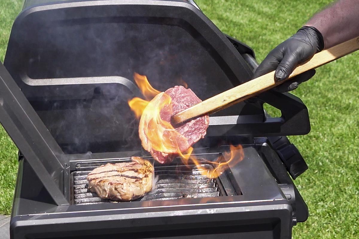 Person wendet ein Stück Fleisch auf einem Grill.