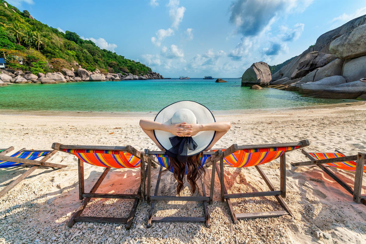 Eine Frau liegt mit Sonnenhut in einem Liegestuhl am Strand.