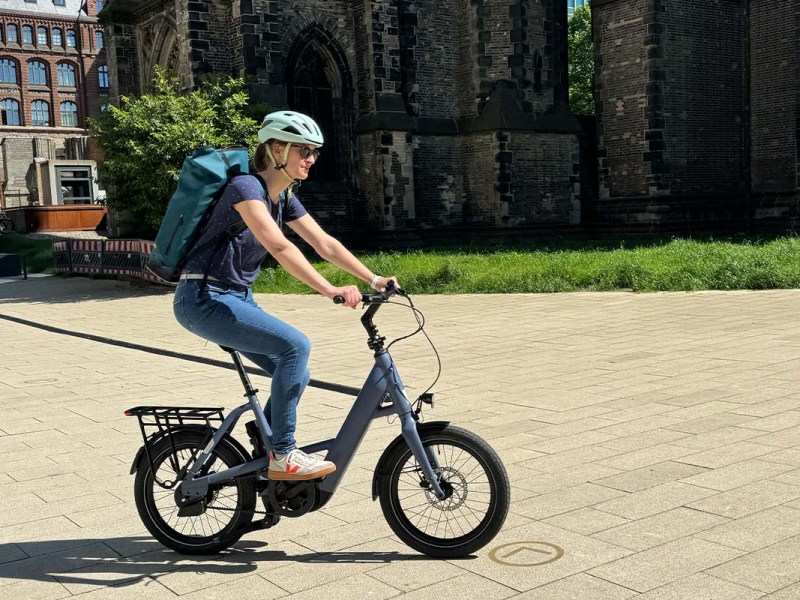 Frau fährt mit einem E-Bike über einen Platz, Kirche im Hintergrund