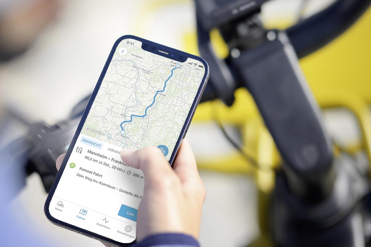 Person mit Smartphone in der Hand neben einem E-Bike.