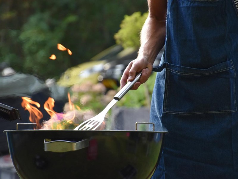 Person steht vor einem Grill unter freiem Himmel.