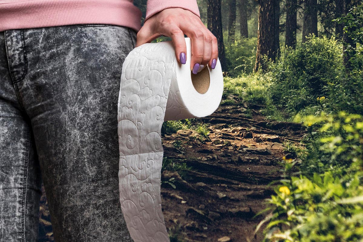 Person mit einer Toilettenrolle in der Hand vor einem Wald stehend.