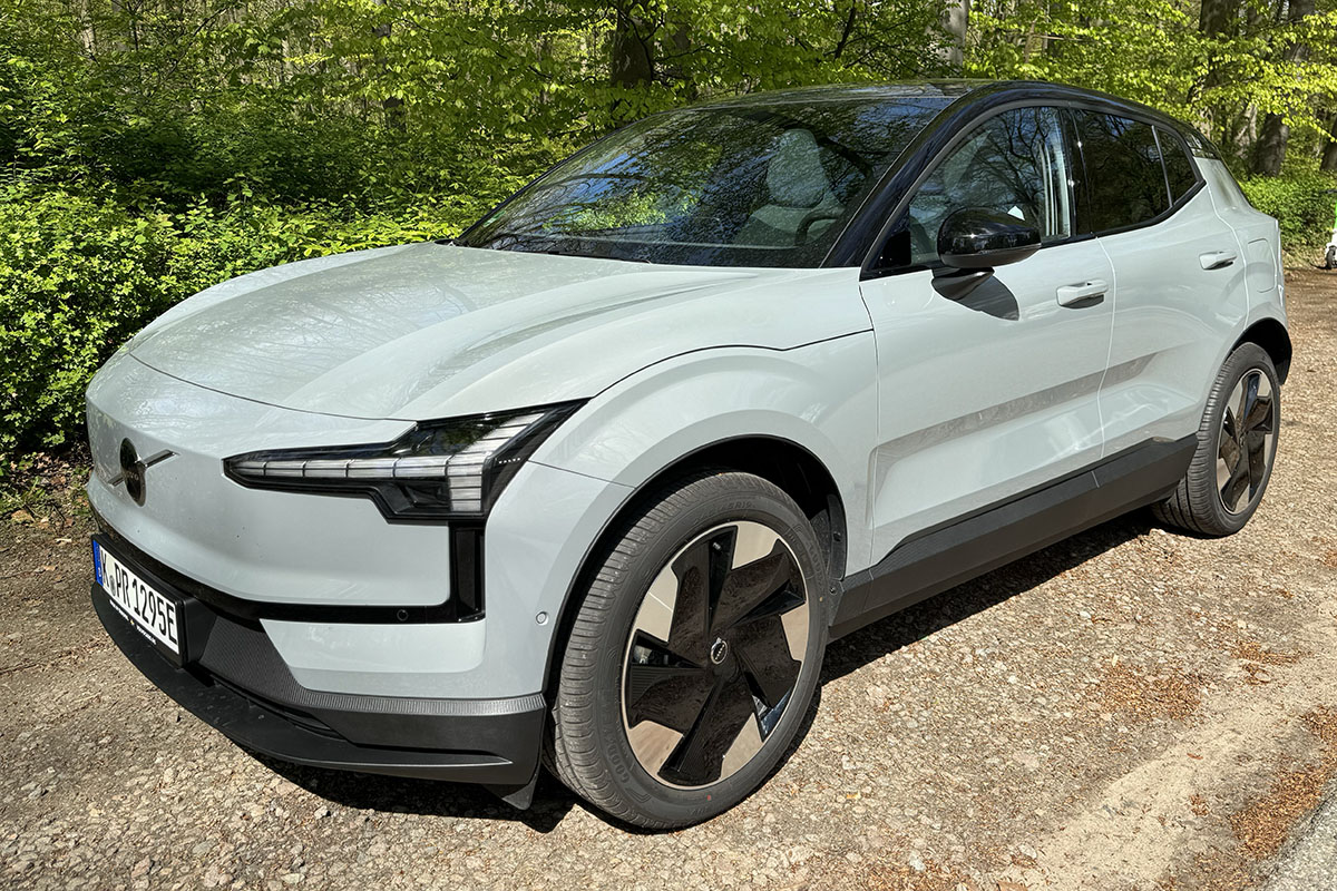 E-Auto Volvo EX30 parkend vor einem Wald von schräg vor aus fotografiert.