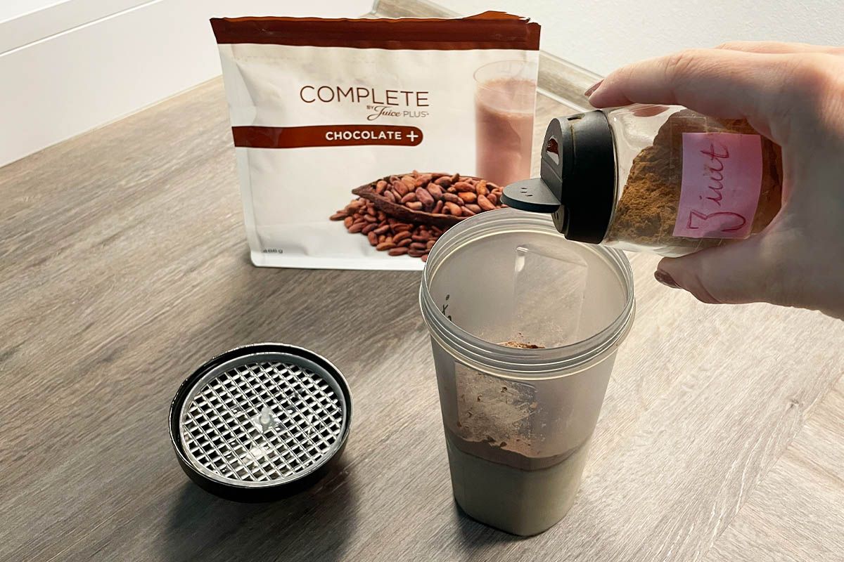 Eine Hand füllt Zimt in den geöffneten Juice Plus+ Shaker.