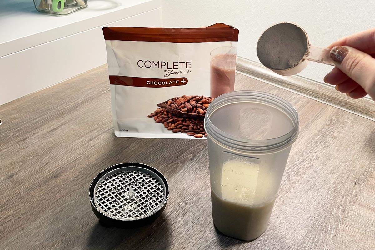 Eine Hand füllt braunes Pulver in den geöffneten Juice Plus+ Shaker.