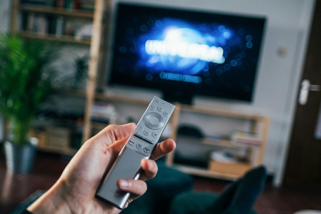 Person mit Fernbedienung in der Hand vor einem Fernseher.