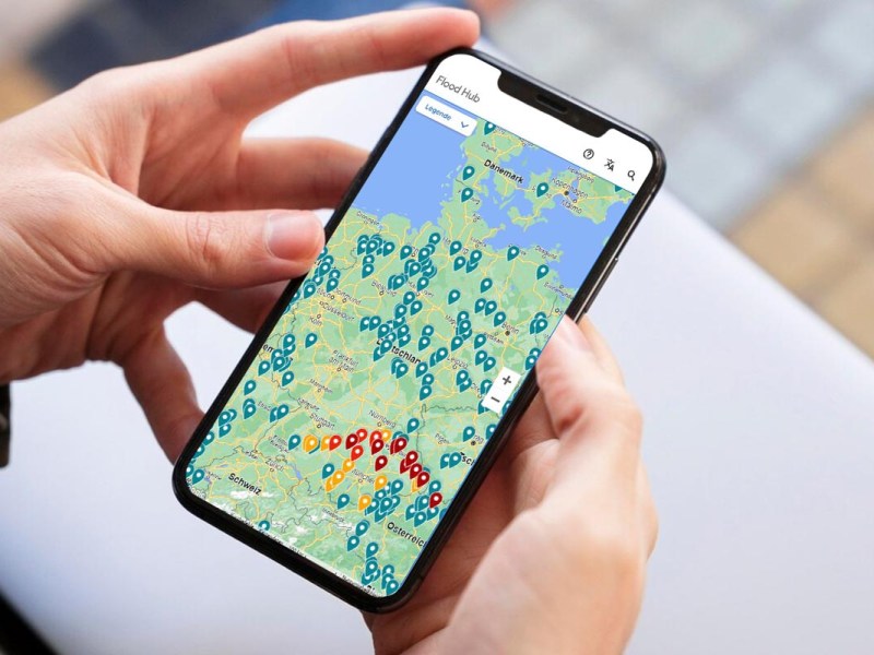 In der Hand gehaltenes Smartphone mit geöffneter "Flood Hub" Website.