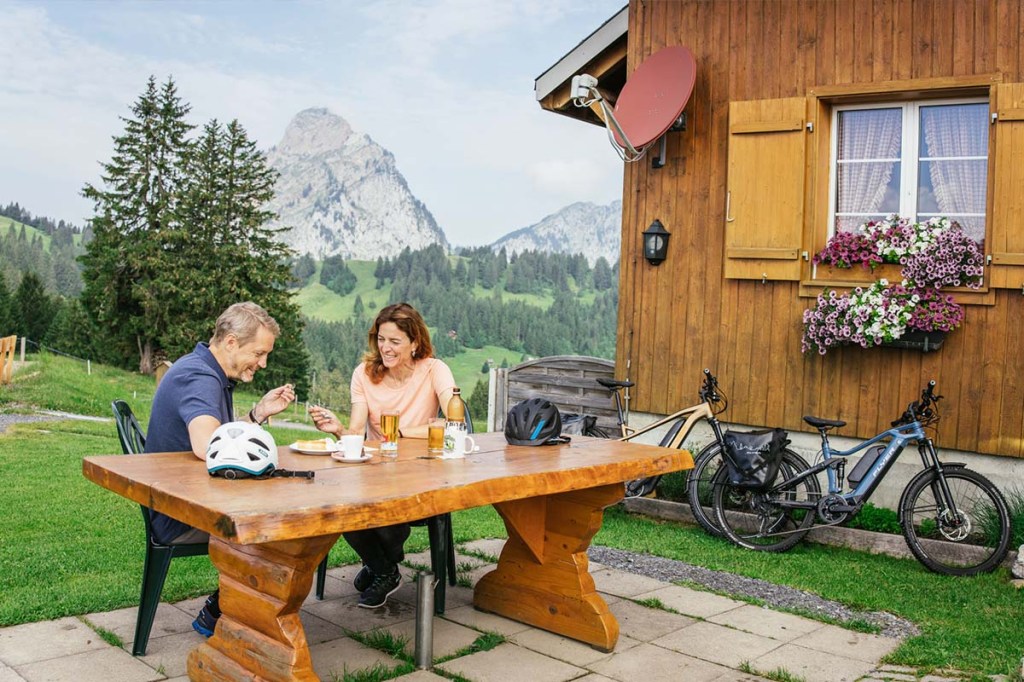 zwei Personen sitzen an einem Holztisch vor einer Holzhütte in der Natur