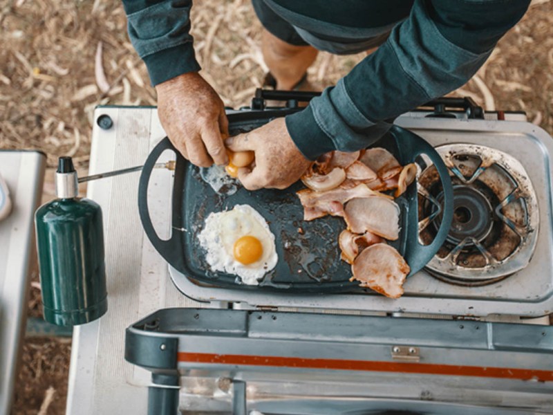 Ein Mann macht rustikale Spiegeleier auf einem Campingkocher.