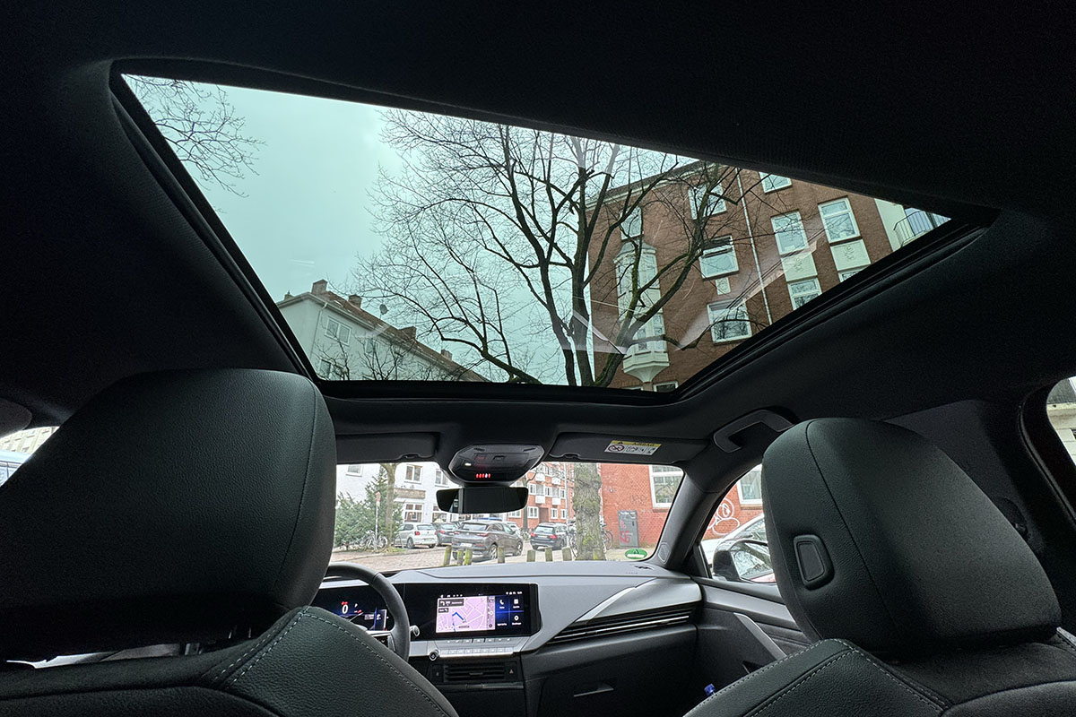 Blick auf Himmel über Wohngebäuden aus Glasdach beim E-Auto Opel Astra Sports Tourer Electric.