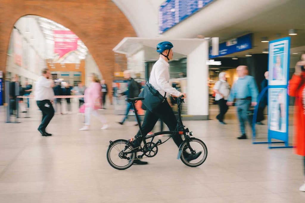 Mann schiebt sein Faltrad durch eine Bahnhofshalle