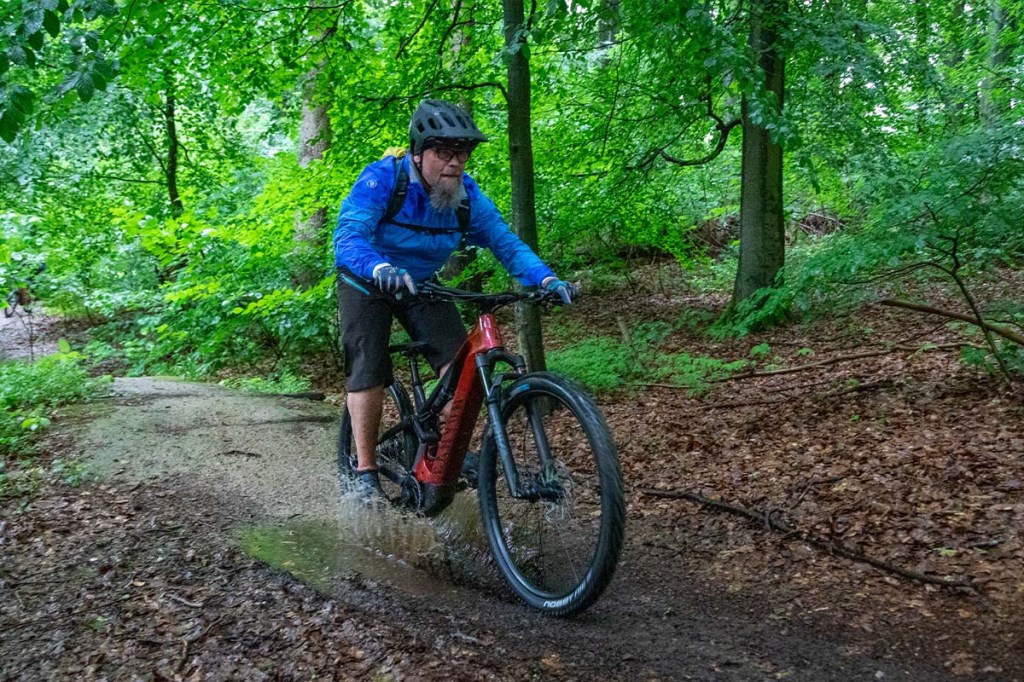 Mann fährt mit einem Mountainbike durch eine Pfütze im Wald