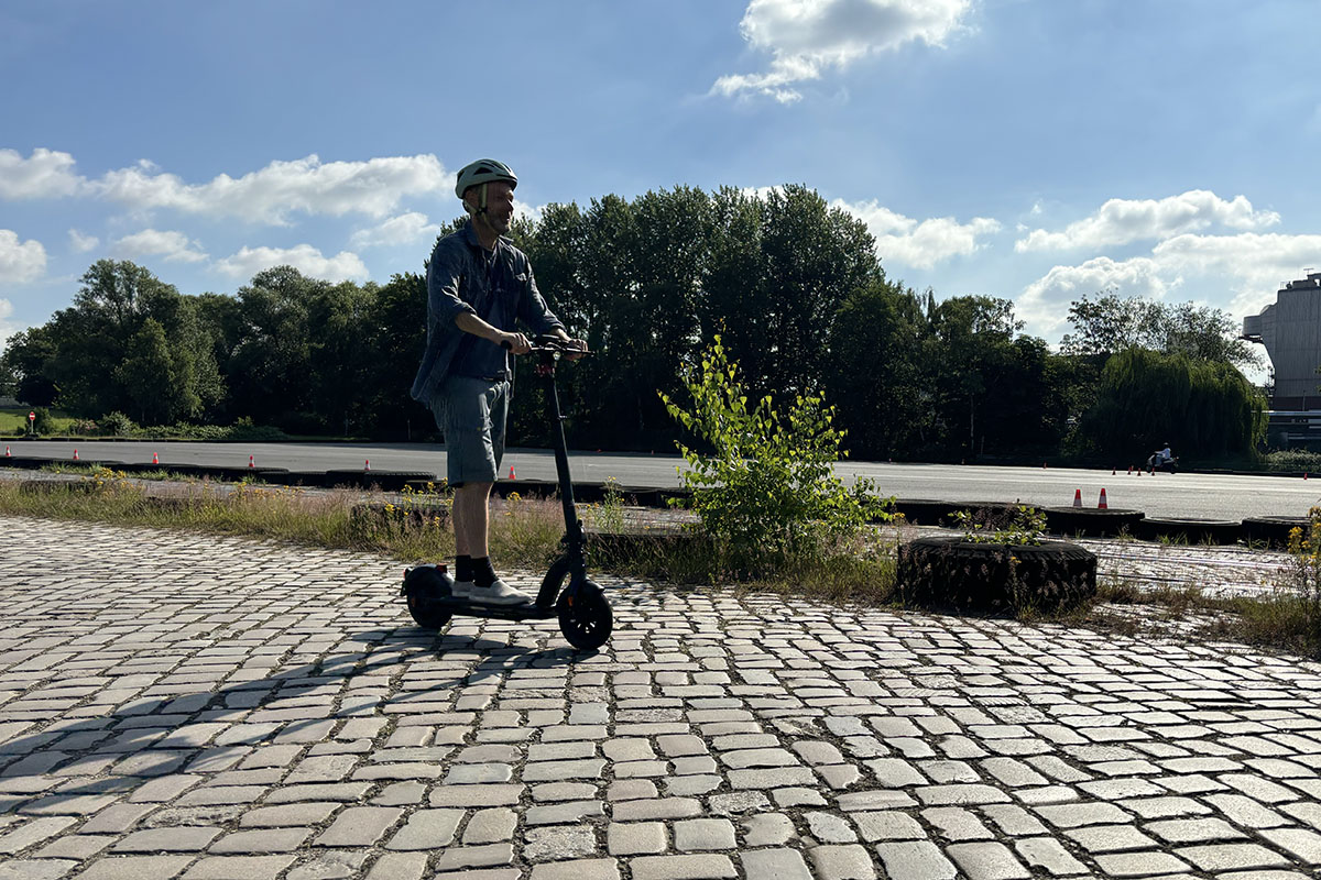 Mann fährt auf einem E-Scooter über Kopfsteinpflaster.