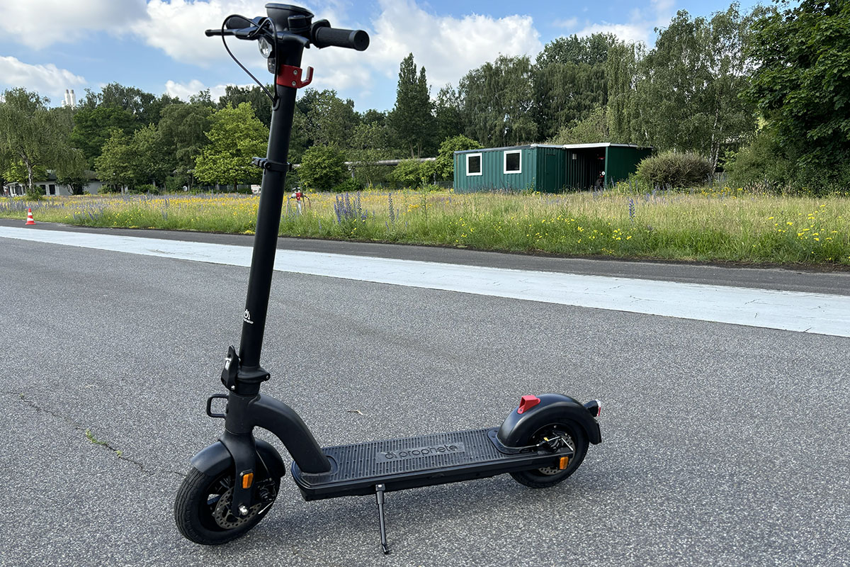 Ein E-Scooter steht im Profil auf einer Straße vor einem Rasenstück.