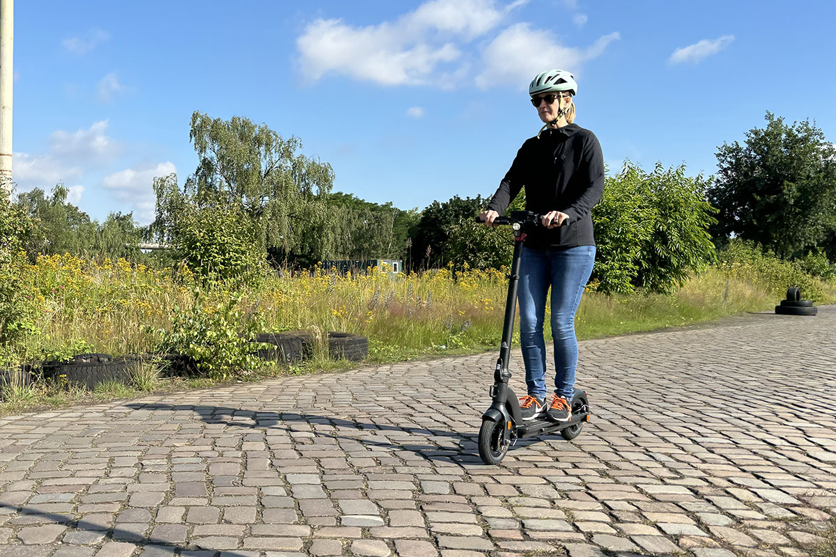 Frau fährt über Kopfsteinpflaster auf E-Scooter.