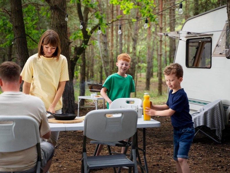 Familie an einem Tisch im Wald neben einem Camper.