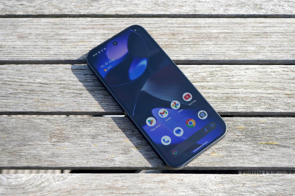 Das Smartphone Google Pixel 9 liegt mit eingeschaltetem Display auf einem Holztisch.