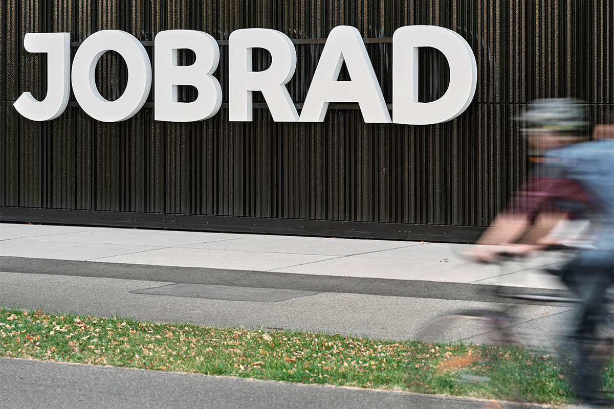 Ein großes JobRad-Logo hängt als Schild an einer Holdwand. Im Vordergrund fährt ein Radfahrer auf einem Fahrradweg.