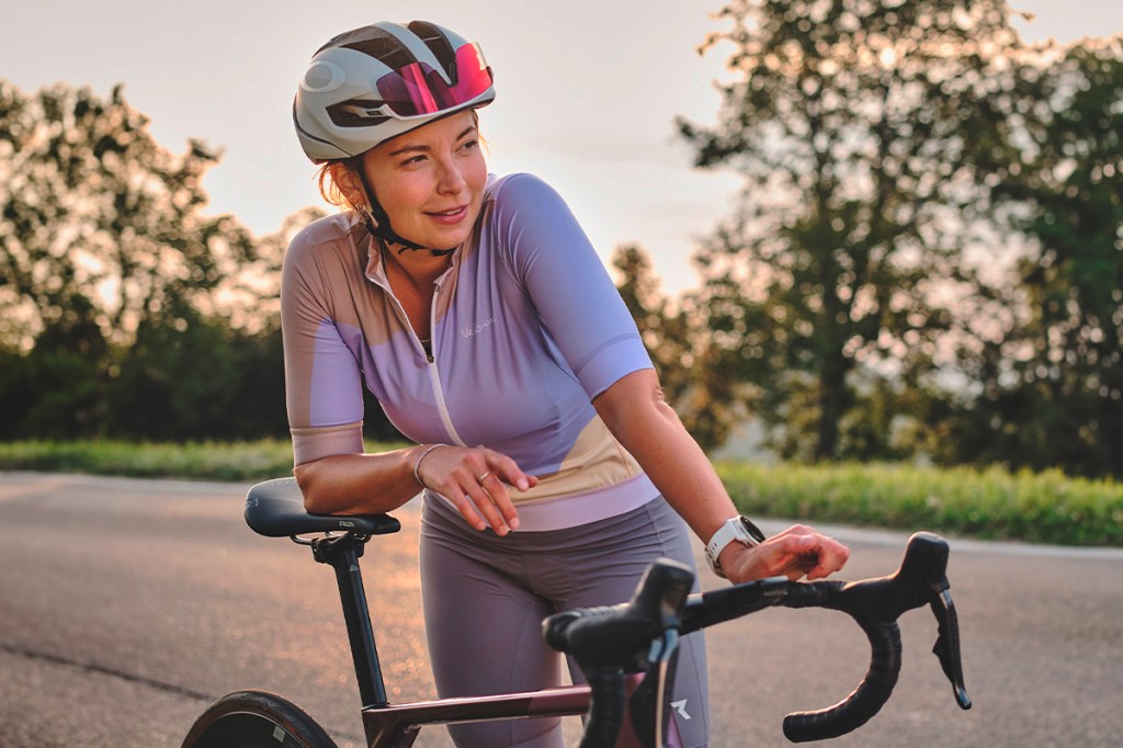 Eine Frau im Radler-Outfit stützt sich im Freien auf eine Rennrad.