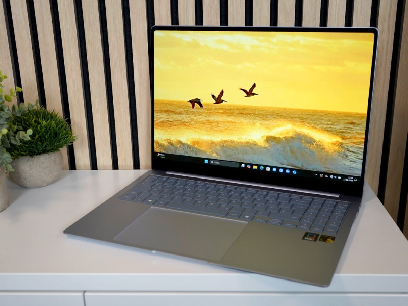 Das Notebook Samsung Galaxy Book 4 Edge steht eingeschaltet auf eine hellen Sideboard vor einer holzverkleideten Wand