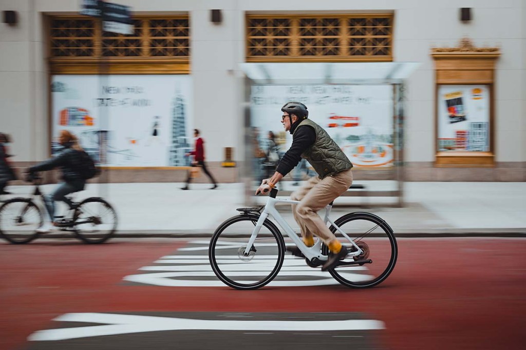 Person fährt mit einem E-Bike eine Straße entlang, städtischer Hintergrund