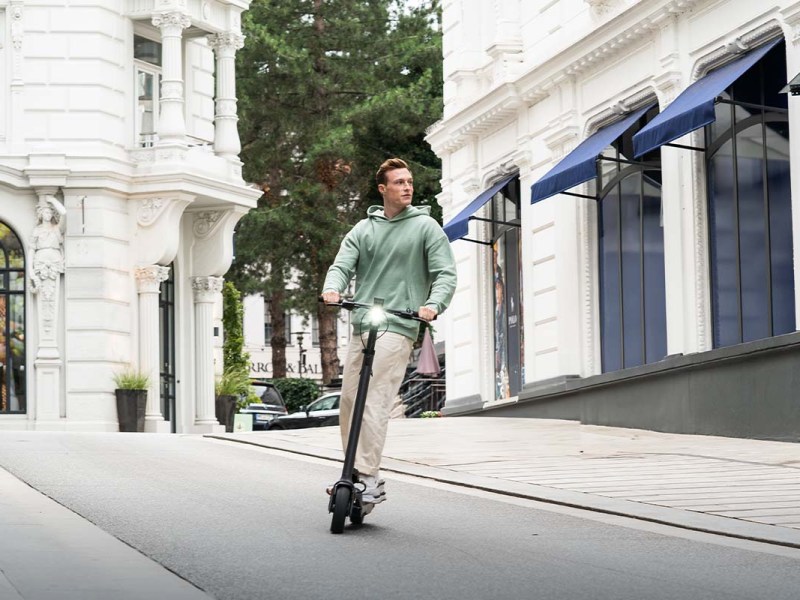 Mann fährt mit einem E-Scooter eine Straße entlang