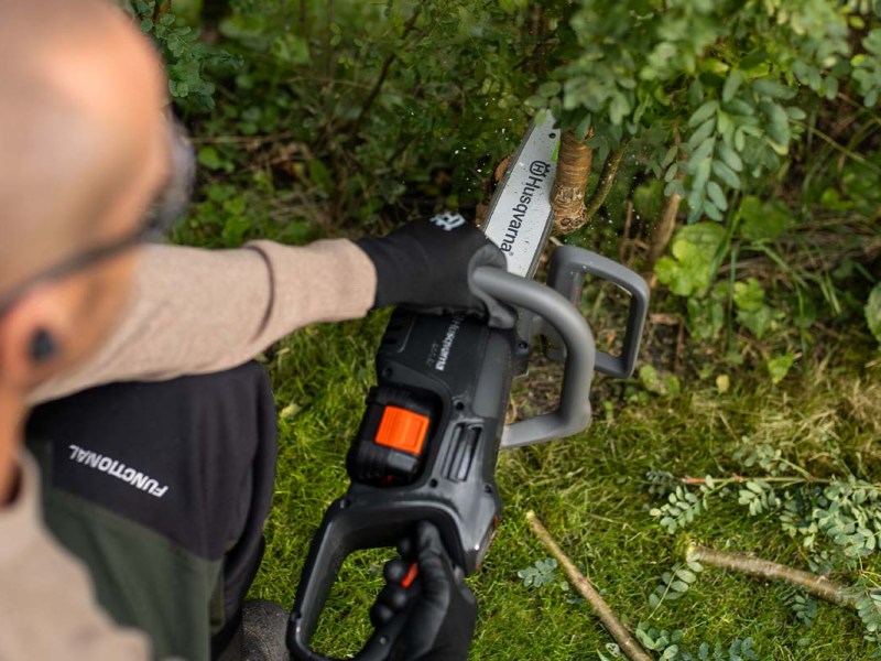 Overshoulder-Blick einer Person mit einer Kettensäge, die einen Ast durchsägt