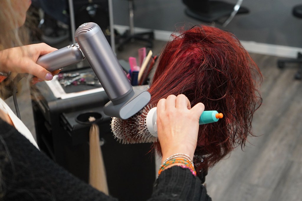 Eine Person föhnt einen lebensgroßen Puppenkopf mit dem Dreame Pocket und dem Anti-Frizz-Aufsatz.