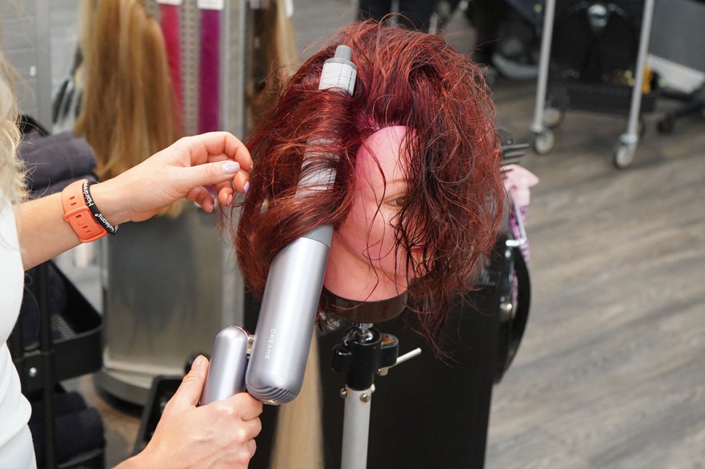 Eine Person macht einem lebengroßen Puppenkopf mit dem Dreame Pocket und dem Lockenstab-Aufsatz Locken.