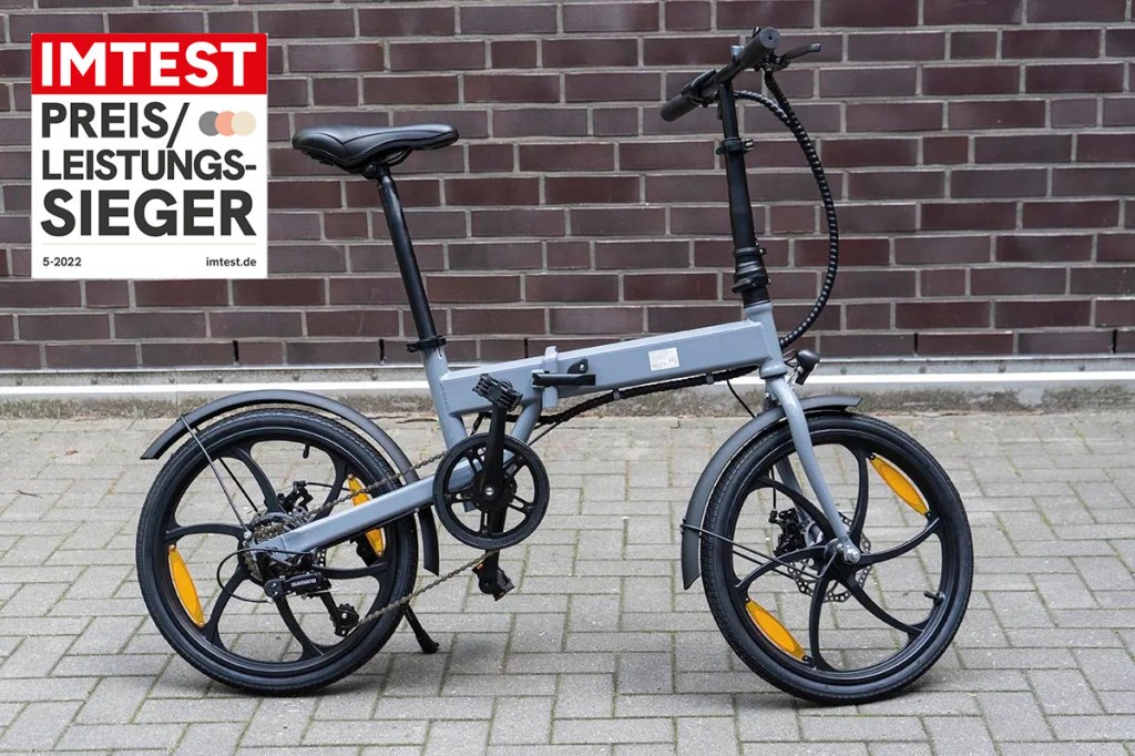 Falt-E-Bike im Profil vor Mauer stehend. Eingeklinkt ein Preis-Leistungs-Sieger-Logo von IMTEST.