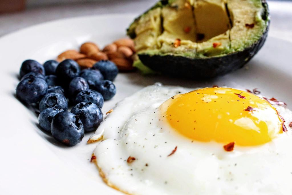 Ein Spiegelei neben einer Avocado, außerdem sind Blaubeeren im Bild. 