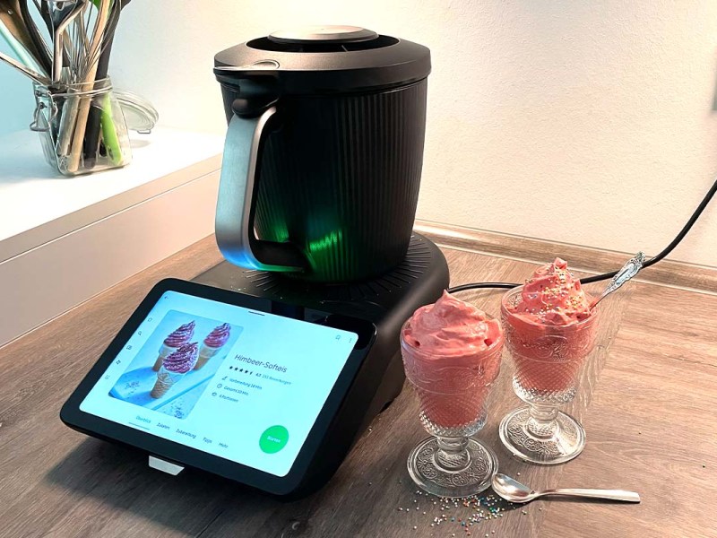 Der Thermomix TM7 mit Mixtopf neben zwei Gläsern mit rosa Softeis und Streuseln.