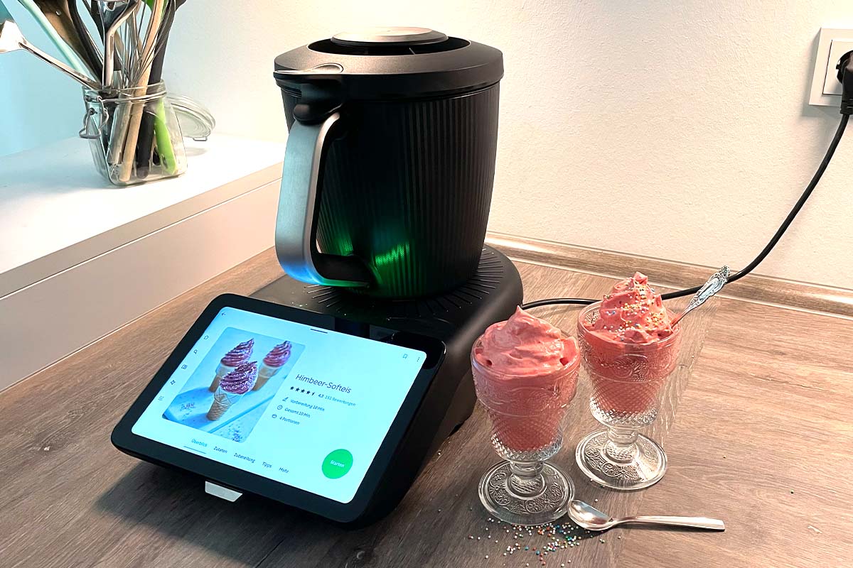 Der Thermomix TM7 mit Mixtopf neben zwei Gläsern mit rosa Softeis und Streuseln.