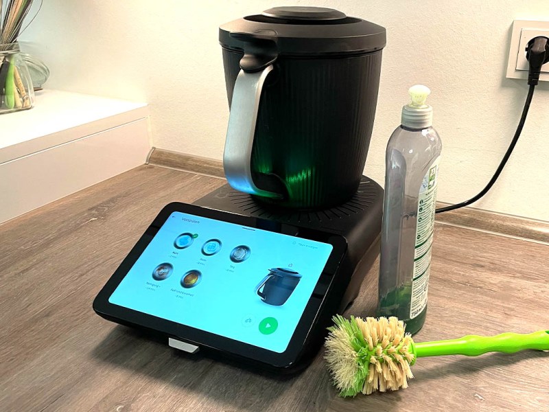 Der Thermomix TM7 in Betrieb. Daneben ein Spülmittel und eine Spülbürste.